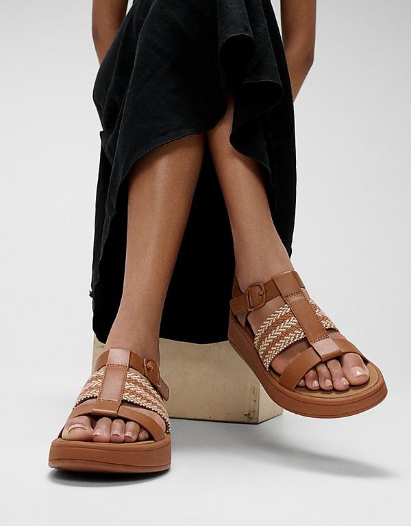 Woman sitting on a stool wearing black skirt and FMODE weave sandals in Tan - From FitFlop EU